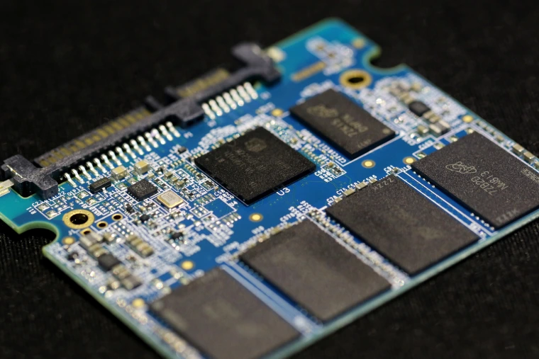 A bare solid-state drive circuit board: a green board with several black flash-memory chips, a controller chip, and a SATA connector along one edge — no moving parts